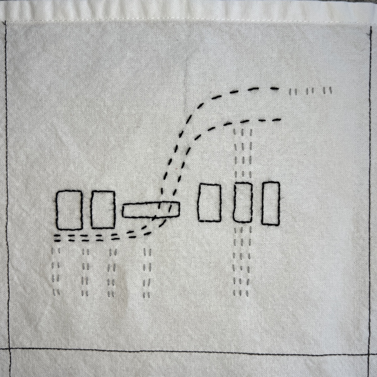 Overhead photo of white fabric 8”x8” square, with black and grey embroidery. Five black outlined rectangles are in a horizontal line in the middle of the square. Two lines swoop from the lower left corner to the upper right corner. Short grey stitches make dashed verticals lines under and through some of the rectangles.