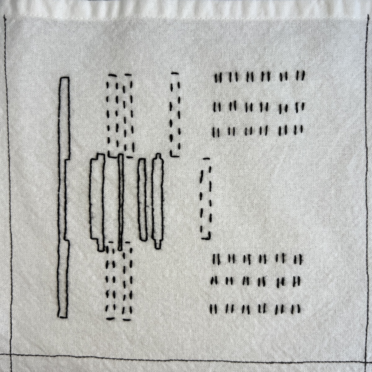 Overhead photo of white fabric 8”x8” square, with black embroidered vertical rectangles in running stitch and backstitch moving across the square, and then short vertical pairs of lines in rows on the right hand side of the square.