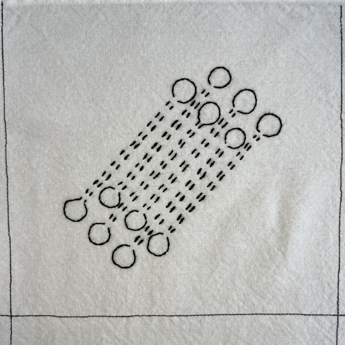 Overhead photo of white fabric 8”x8” square with 5 sets of diagonal lines in running stitch with circles on the end of each line.