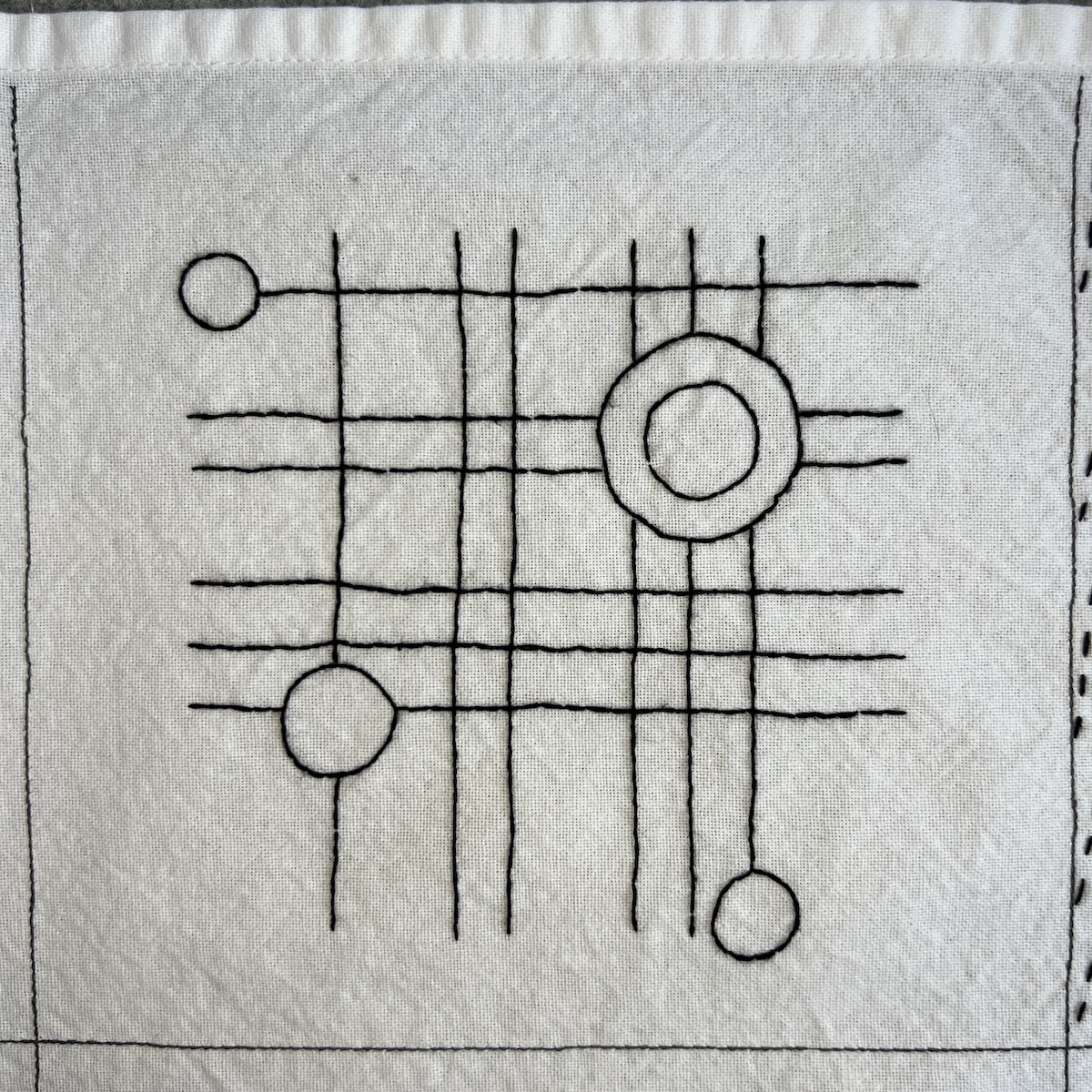 Overhead photo of white fabric 8”x8” square with a grid of thin lines embroidered in black thread. A few circles of different sizes are stitched over the grid.