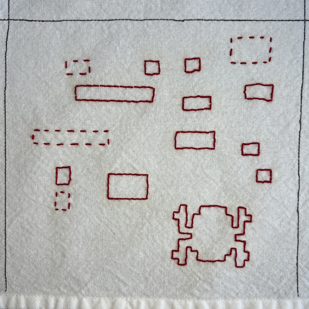 Overhead photo of white fabric 8”x8” square, with a series of red embroidered outlined squares and rectangles scattered throughout the panel. In the bottom right corner is a pixelated frog shape outlined in red.