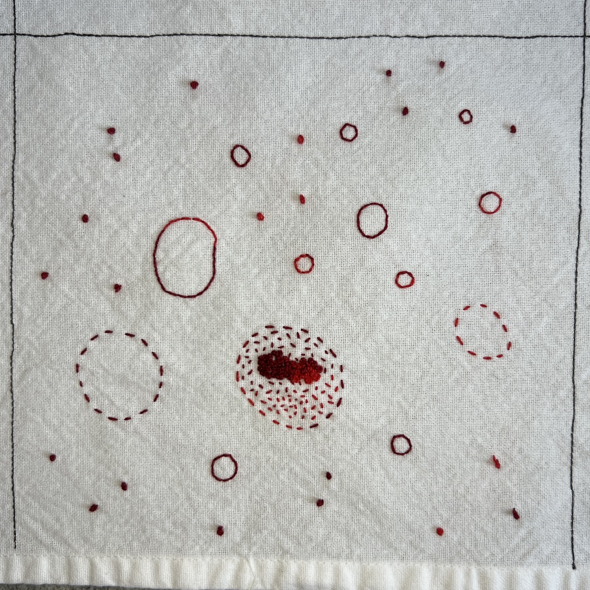 Overhead photo of white fabric 8”x8” square, with different sizes of circles and French knots stitched in red variegated thread.