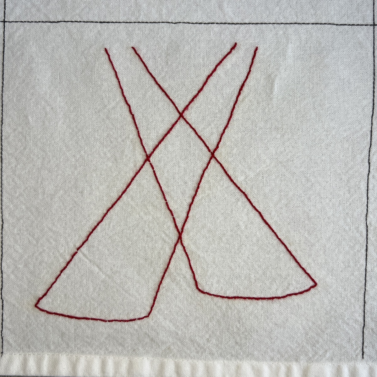 Overhead photo of white fabric 8”x8” square. Red thread is embroidered into what looks like two crossing beams of light.