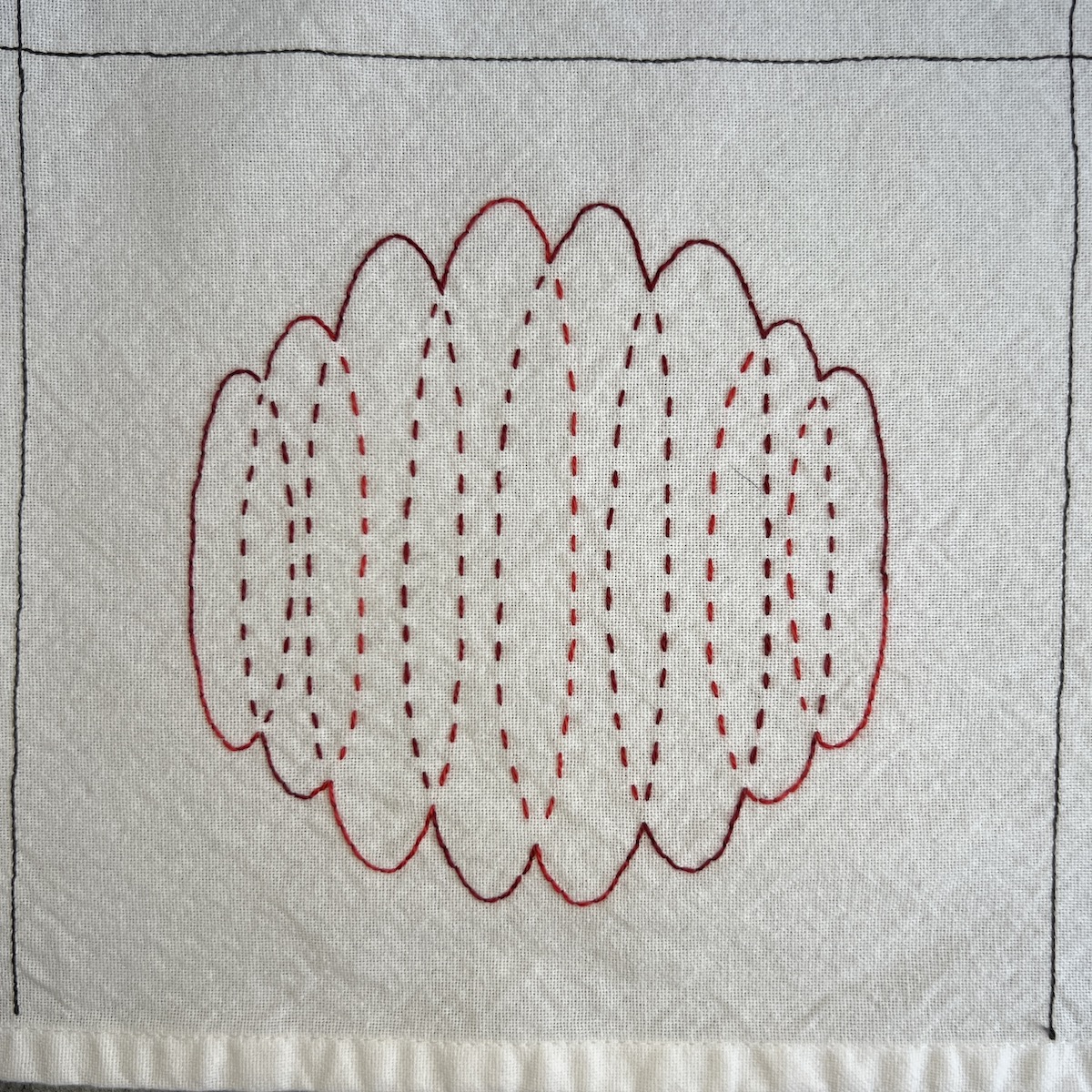 Overhead photo of white fabric 8”x8” square. 8 vertical ovals embroidered in red variegated thread overlap as they span the width of the square. The ovals are longest in the middle and decrease in size as they extend to the edges.