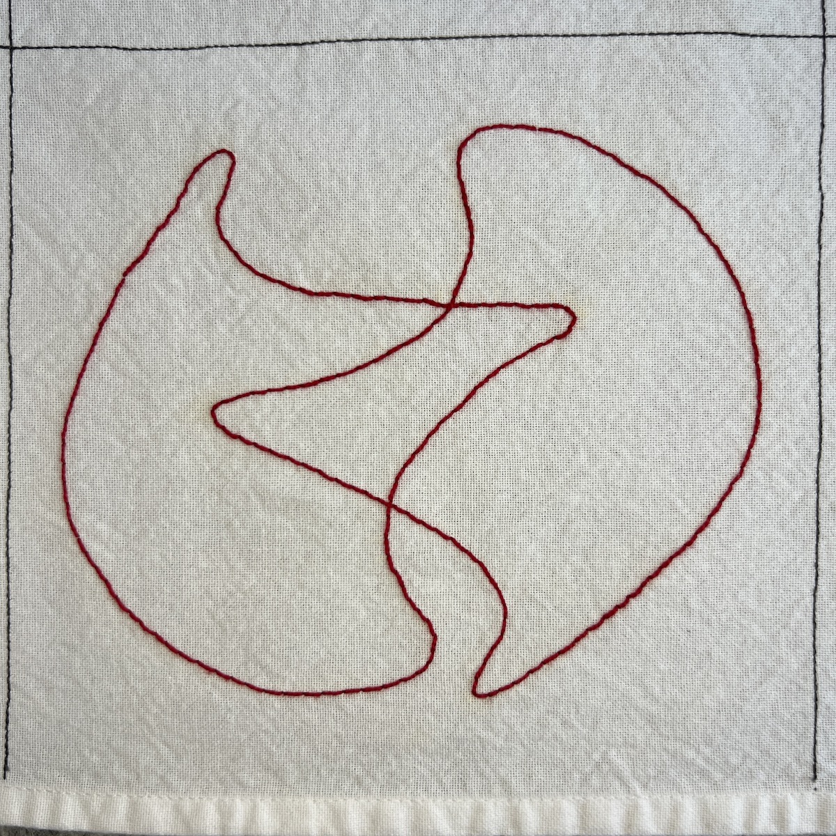 Overhead photo of white fabric 8”x8” square with 2 overlapping abstract rounded shapes in red embroidered lines, making an orb shape.