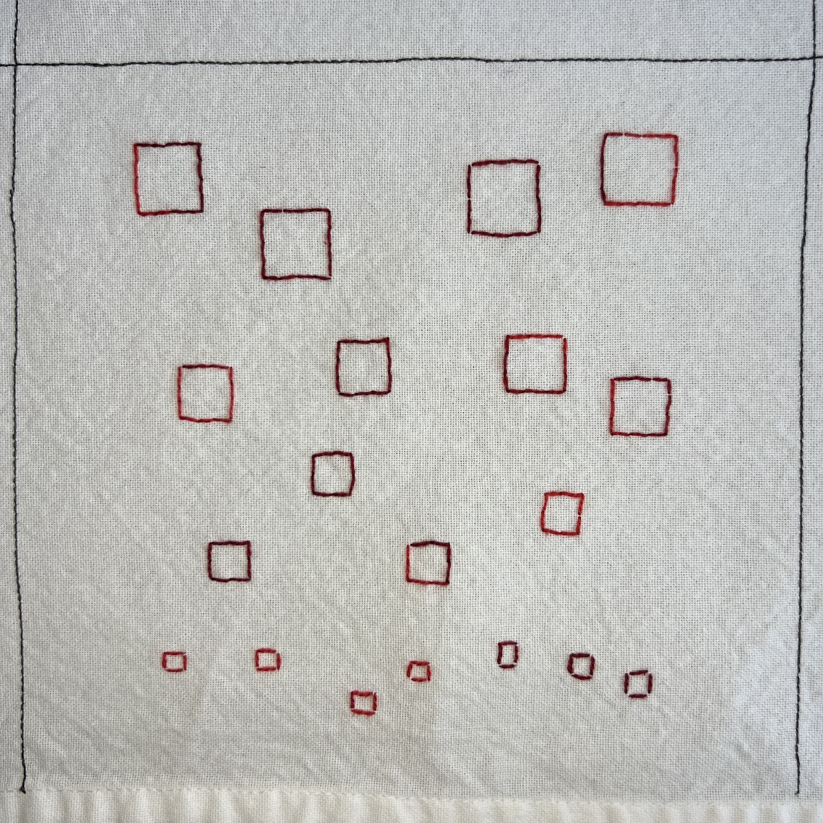 Overhead photo of white fabric 8”x8” square, with a series of variegated red embroidered squares scattered, decreasing in size from the top to the bottom of the panel.